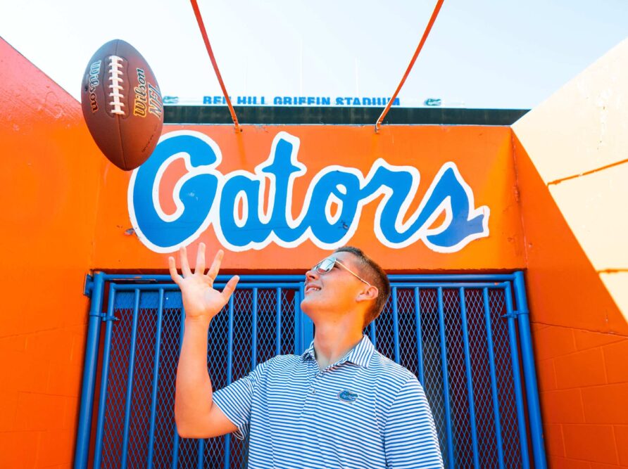 University of Florida student tossing a football in front of a Gators sign