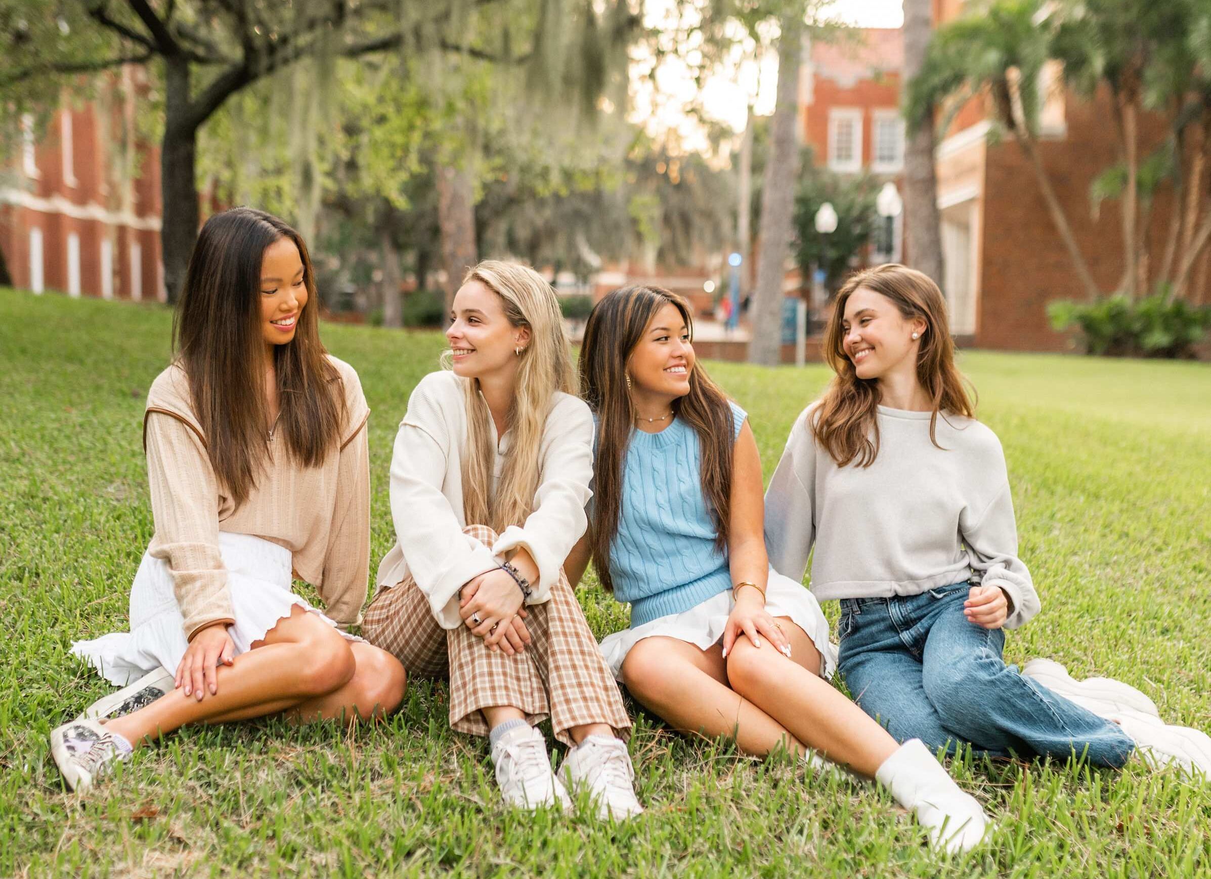 Four UF roommates matched to live together at Sweetwater sit on the lawn on campus