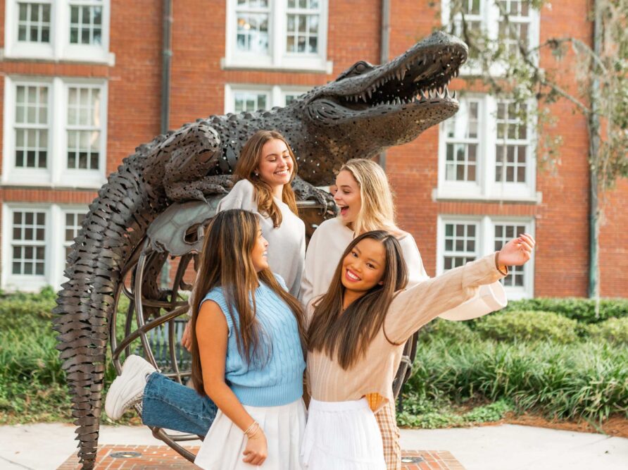 four girls hug in front of the gator statue at UF
